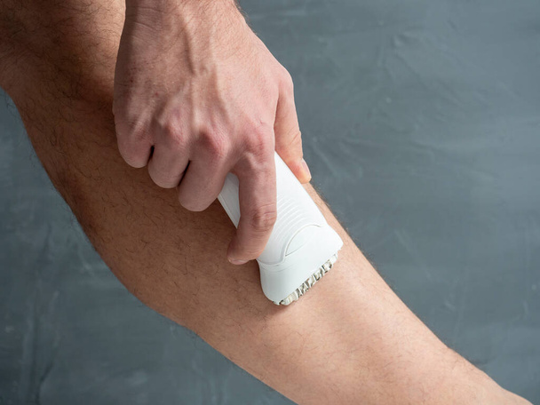 Close-up of a man removing hair from his leg using an electric depilator. Lots of leg hair. The concept of skin care and men's beauty - Foto, imagen