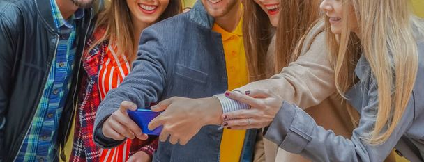 Группа друзей, стоящих у стены и наслаждающихся друг другом подростки, используя смартфон и улыбаясь, пытаясь сделать селфи-технологию - Фото, изображение