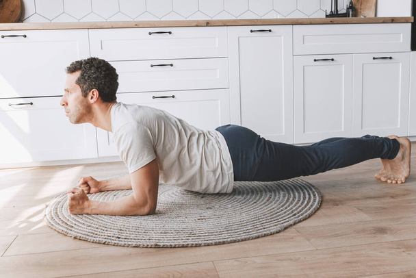 young man in white t-shirt exercising  on floor in kitchen - 写真・画像