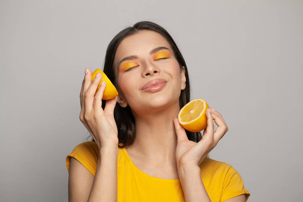 Attraktive Frau mit klarer Haut genießt Zitronenfrüchte auf weißem Hintergrund. Ernährungs-, Haut- und Gesichtsbehandlungskonzept - Foto, Bild