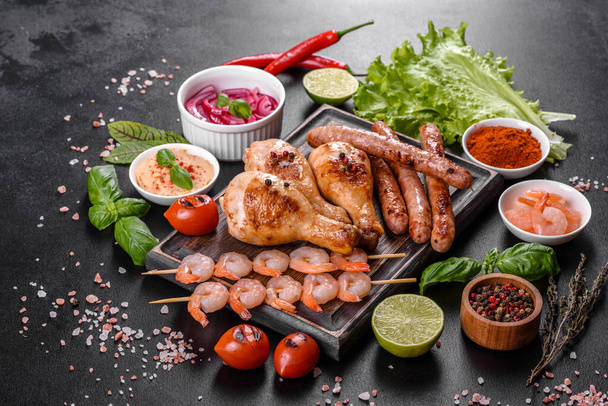 Composition of sausages, chicken, pork and shrimp prepared on grill, as well as vegetables prepared on grill with spices and herbs. Cooking on fire - Photo, Image