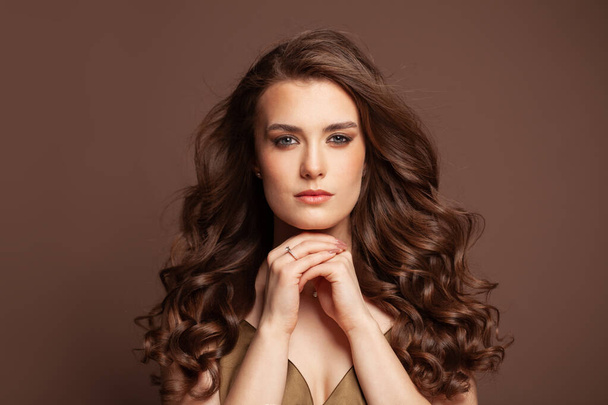 Hermosa modelo de cabello de mujer con pelo largo y sano rizado oscuro sobre fondo marrón - Foto, imagen