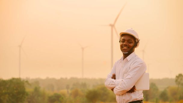 Ingegnere africano mulini a vento con cappello rigido bianco e utilizzando tablet con turbina eolica sul tramonto silhouette - Foto, immagini