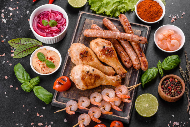 Composition of sausages, chicken, pork and shrimp prepared on grill, as well as vegetables prepared on grill with spices and herbs. Cooking on fire - Photo, Image