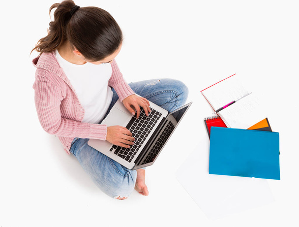 Young female student sitting with crossed legs working with a laptop, isolated over white background - 写真・画像