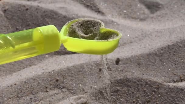 Żółty piasek zabawki przesiewacz w kształcie serca z wylewania ziaren piasku na plaży - Materiał filmowy, wideo
