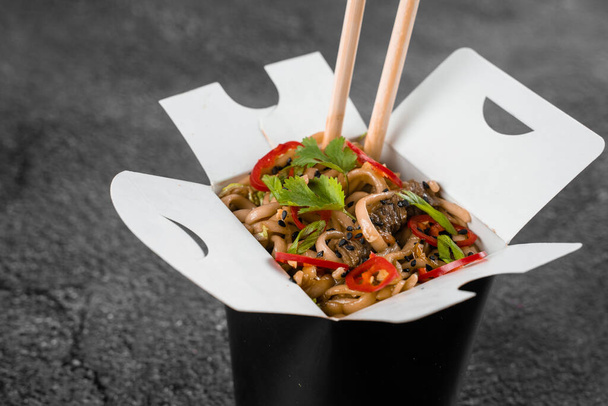 Wok σε κουτί πικάντικα noodles σε μαύρο δοχείο τροφίμων. Υπηρεσία παράδοσης γρήγορου φαγητού. Χοιρινό κινέζικο γεύμα στο δρόμο - Φωτογραφία, εικόνα