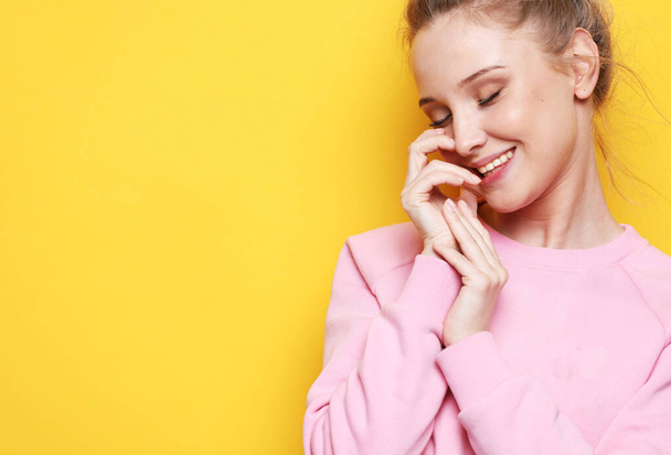Portrait of young blonde positive female with cheerful expression, dressed in pink sweater, over yellow background. Close up. - Foto, Imagem