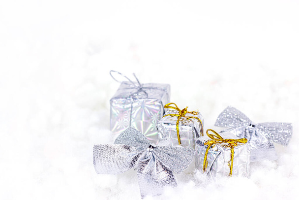 Bright silver Xmas decorations (ribbons, presents, gift boxes) on white artificial snow background with copy space. Christmas and New Year traditional holiday celebration concept. - Photo, Image