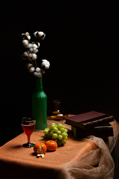 Still life with fruits and books in dark environment. vases, cup and tulle fabric - 写真・画像