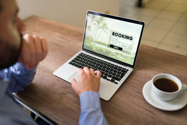 Sales representative typing on his laptop and looking at booking information at his office desk. Travel agent planning a vacation trip for a customer - Photo, Image