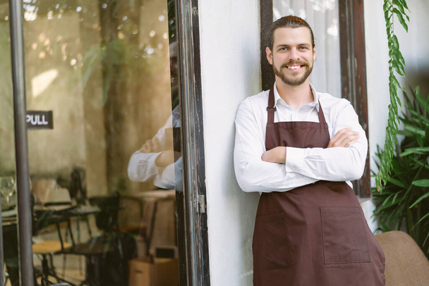 Handsome and confident cafe owner standing with his arms crossed at coffee shop door. Caucasian man with beard standing in front a cafe looking at camera. Startup small business owner concept. - Foto, afbeelding