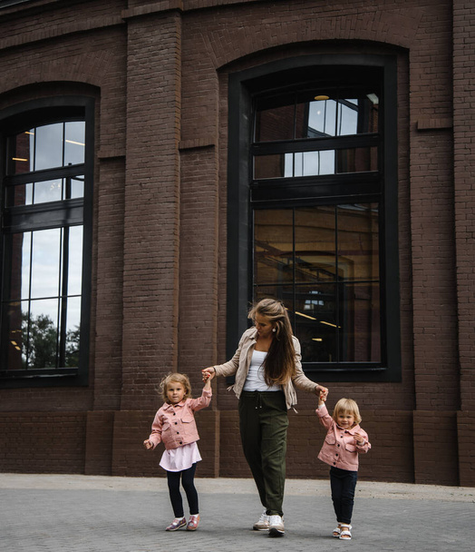young beautiful mother with long hair with children on walk in street happiness joy fun motherhood - Photo, image