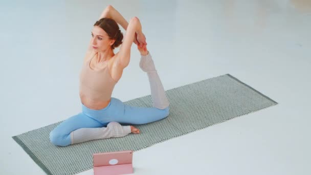 Mujer joven se dedica a la formación en línea. La mujer atlética haciendo yoga en el suelo - Imágenes, Vídeo