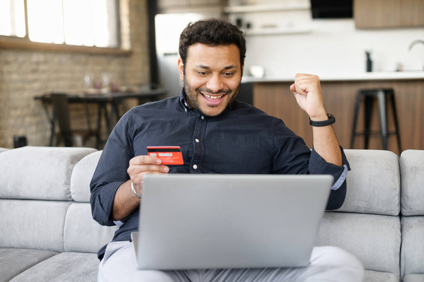 Happy indian guy holding credit card and paying online - Photo, Image