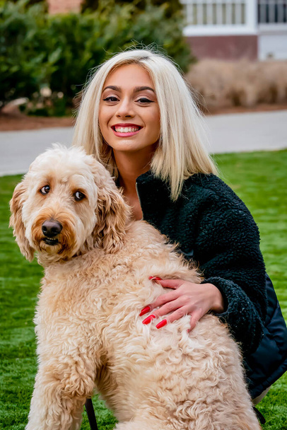 Una hermosa modelo rubia joven posa al aire libre con su cachorro joven - Foto, imagen
