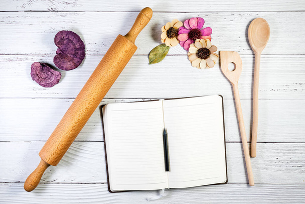 A notebook copy space mockup styled in a kitchen or bakery setting, with a rolling pin and wooden spoons on a wooden surface - Photo, Image