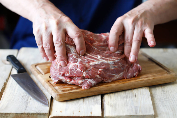 Nyers hús a séf kezében egy fa deszkán. Főzőhús. - Fotó, kép