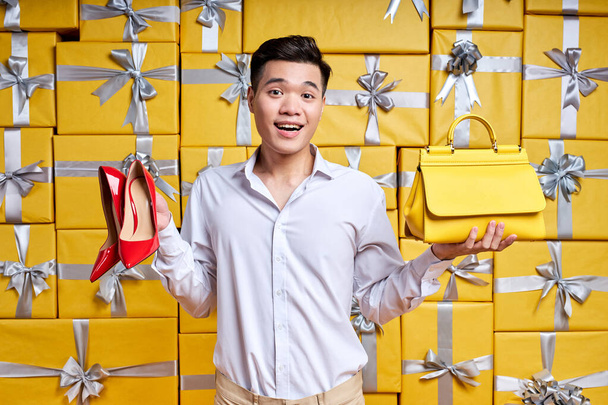 Asian man offers purchase options, holding shoes and handbag in hands - Photo, image
