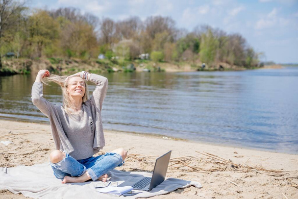Heureuse femme libre avec ordinateur portable sur la plage au bord du lac. - Photo, image