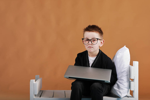 schoolboy in glasses closing laptop sitting on bed. Child doing school homework and tired looking on camera. Online learning, distance lesson, education with online tutor at home isolation. - Фото, изображение