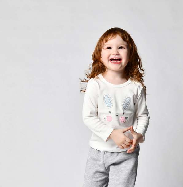 Charming smiling red-haired little girl in sportswear studio shot - Foto, afbeelding