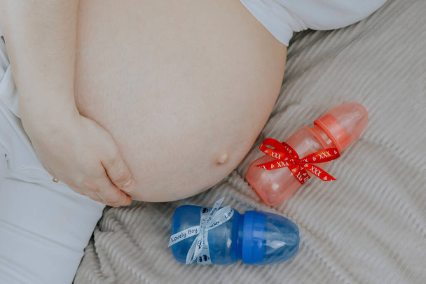 Une femme enceinte tient son ventre avec sa main, et à côté d'une bouteille de lait, vue de dessus, gros plan. - Photo, image