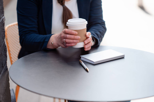 mujer sosteniendo taza de café en la cafetería y portátil con pluma en la mesa - Foto, Imagen