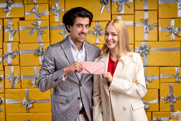male in gray suit giving gift certificate to woman while standing against background full of gtift boxes - 写真・画像