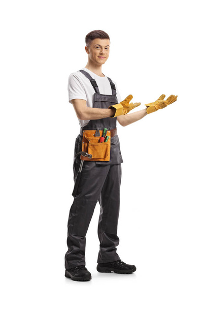 Full length portrait of a young repairman with a tool belt gesturing welcome isolated on white background - Φωτογραφία, εικόνα