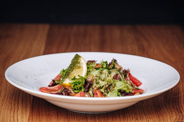 White Plate with Salad Stands on a Wooden Table in a Restaurant - Photo, image