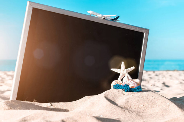ビーチの背景。ヒトデ、貝殻、おもちゃの飛行機、海の自然ビーチの黒板の近くの地球。夏休みのコンセプトのデザイン - 写真・画像