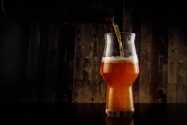 Pouring beer into the glass from the bottle on wooden background. - 写真・画像