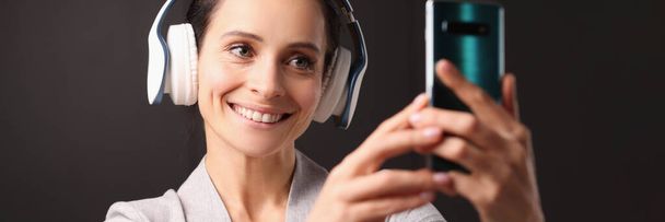 Χαμογελαστή γυναίκα στα ακουστικά ψάχνει σε smartphone - Φωτογραφία, εικόνα