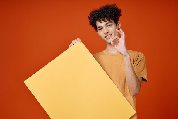 Cheerful man with curly hair poster in hands advertising studio - Foto, afbeelding