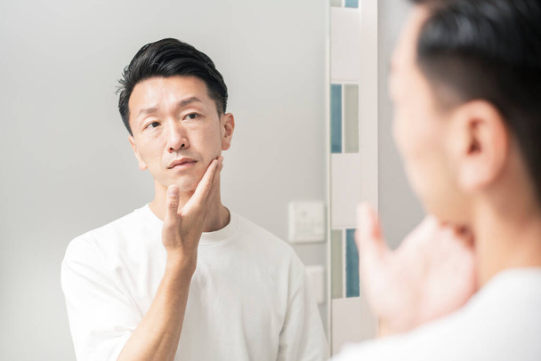 Un uomo che si guarda allo specchio e controlla le condizioni della sua pelle - Foto, immagini
