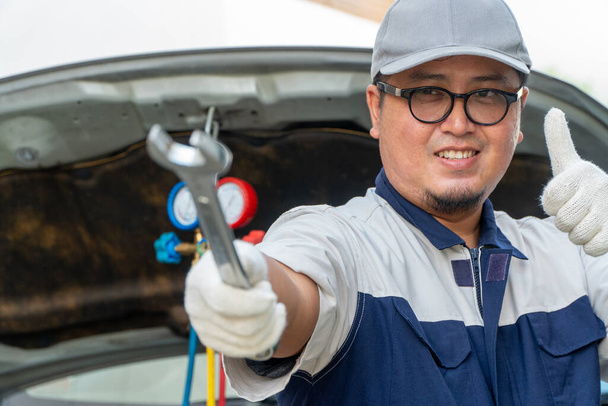 Retrato de un mecánico de automóviles sosteniendo una llave inglesa en un taller de reparación de automóviles. Concepto de reparación de máquinas - Foto, imagen