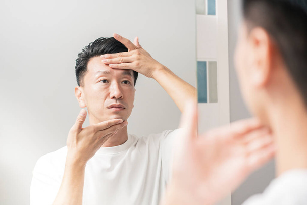 Человек, который смотрит в зеркало и проверяет состояние своей кожи - Фото, изображение