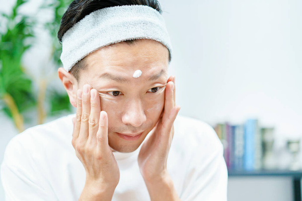 Homens aplicando creme hidratante em seu rosto na sala - Foto, Imagem