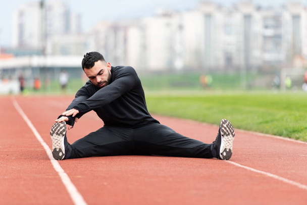 Sporty Man Stretching and Warming Up Legs for Running Fitness Workout on Track Exercising Outside - Foto, Imagen
