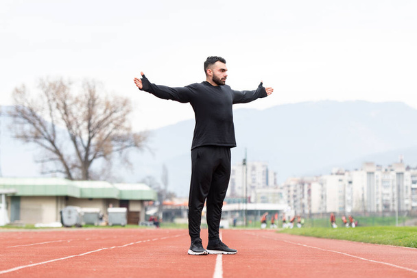 Sporty Man Stretching and Warming Up Legs for Running Fitness Workout on Track Exercising Outside - 写真・画像