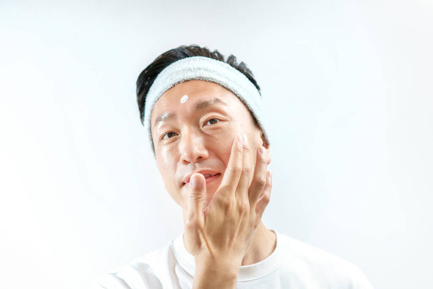 Un homme qui applique de la crème sur son visage et son fond blanc - Photo, image