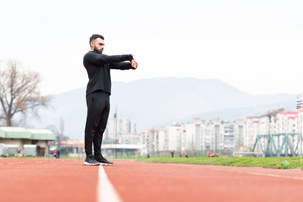 Sporty Man Stretching and Warming Up Legs for Running Fitness Workout on Track Exercising Outside - 写真・画像