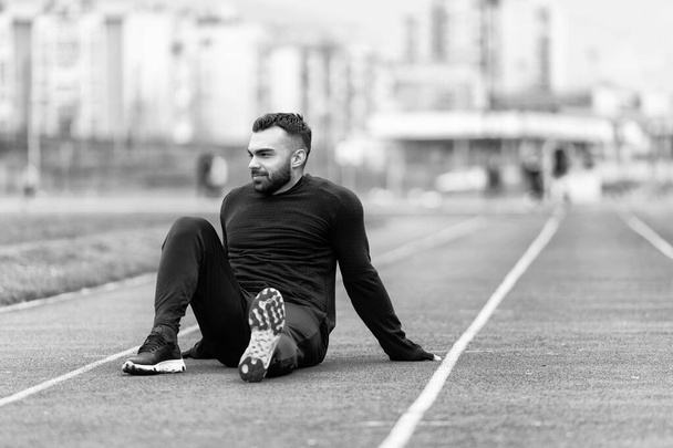 Человек растягивая ноги сломав расслабление после бега устали - отдых тренировки Спорт Здоровый образ жизни спортсмен - Фото, изображение