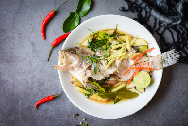 Ψάρι στον ατμό με σάλτσα σόγιας κινέζικο στυλ τροφίμων, ψάρι στον ατμό σε λευκό πιάτο με τζίντζερ τσίλι βότανο και μπαχαρικά λεμόνι lime σε σκούρο φόντο - Φωτογραφία, εικόνα