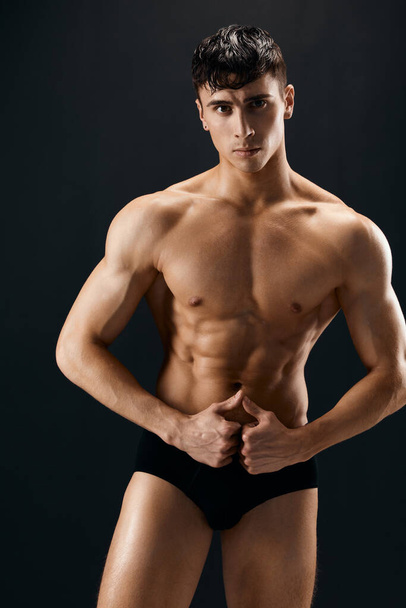 przystojny mężczyzna z muskularny ciało w ciemny w szorty stwarzające odizolowane tło - Zdjęcie, obraz