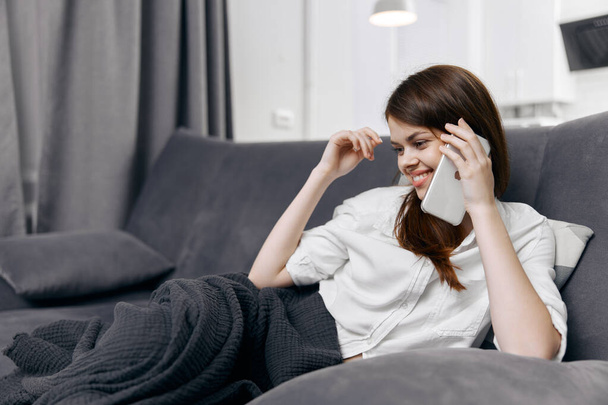 femme parlant au téléphone dans une chambre confortable se cachant avec une couverture sur le canapé - Photo, image