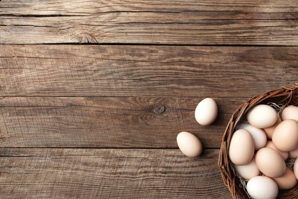 Βιολογικά αυγά κοτόπουλου στο καλάθι σε ξύλινο φόντο. Οργανική έννοια νοικοκυριού με αυγά από όρνιθες ελεύθερης βοσκής και βοσκότοπους - Φωτογραφία, εικόνα