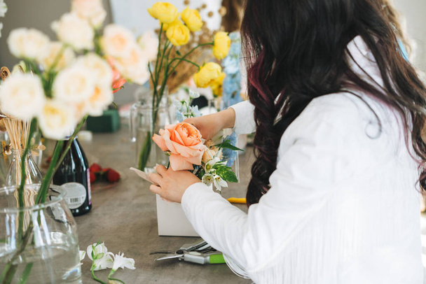 Young woman florist in white with bouquet of flowers in box in flower shop, small local business owner. Young stylish success millennial woman on creative work, working moment - Photo, Image