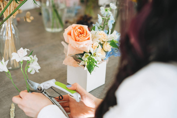 Молода жінка-флорист в білому кольорі з букетом квітів у коробці в квітковому магазині, маленький місцевий власник бізнесу. Молода стильна успішна тисячолітня жінка на творчій роботі, робочий момент
 - Фото, зображення